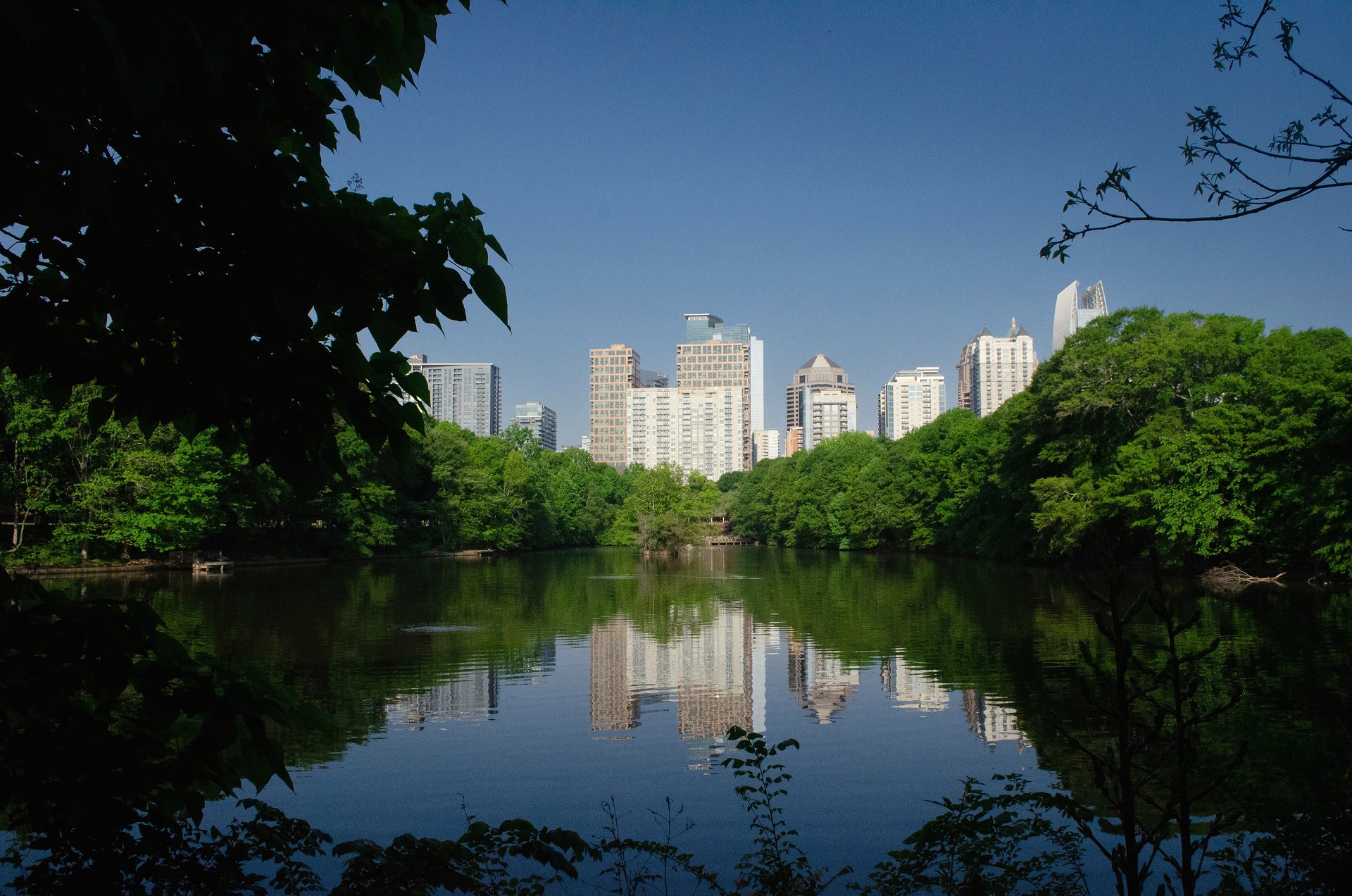 The Midtown Atlanta skyline reflected in a still lake, framed by dense green trees